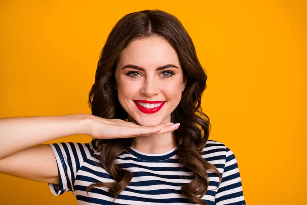 Pretty young woman places her hand under her chin, showing off her smile after full-mouth rehab with her prosthodontist