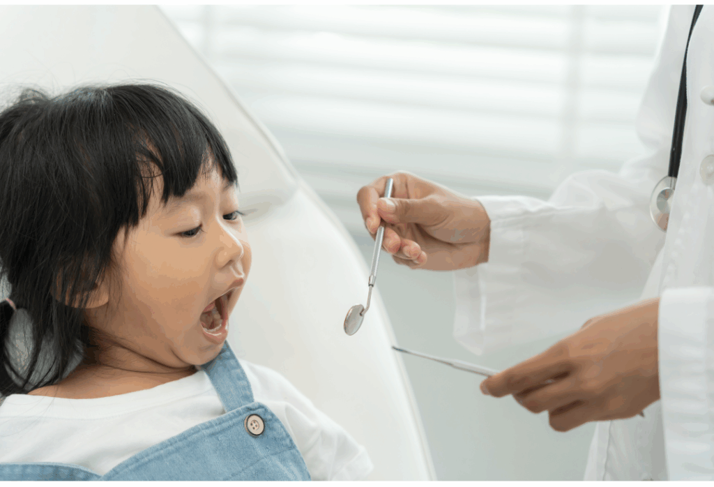 A happy young child opening her mouth for a friendly San Jose pediatric dentist during a routine check-up at Manassra Dental.