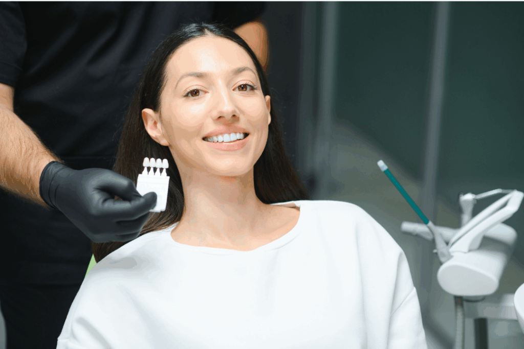 Smiling woman and San Jose cosmetic dentist matching tooth shade for whitening or veneers using a shade guide at Manassra Dental.