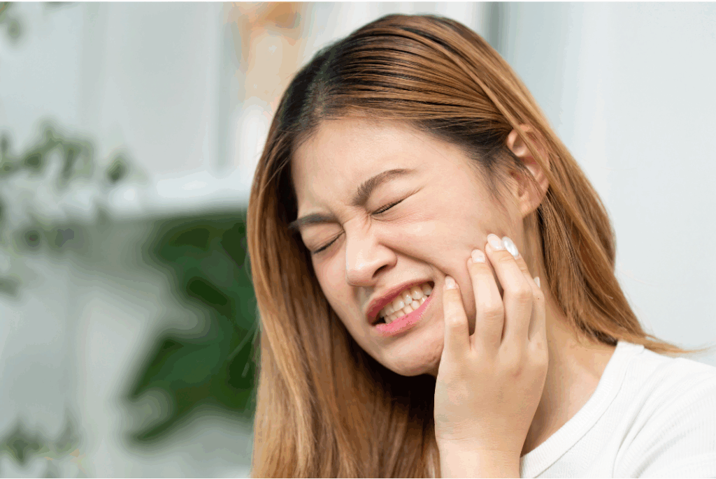 Young woman grasping her cheek in severe pain from a toothache, highlighting the need for immediate **dental pain relief** and emergency care at Manassra Dental in San Jose.