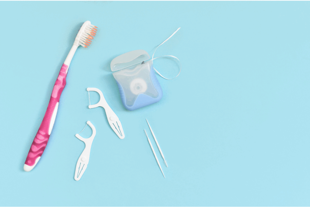Toothbrush, floss, and dental picks on a blue background, representing the daily oral hygiene necessary for **preventing a dental emergency** and maintaining health at Manassra Dental in San Jose.