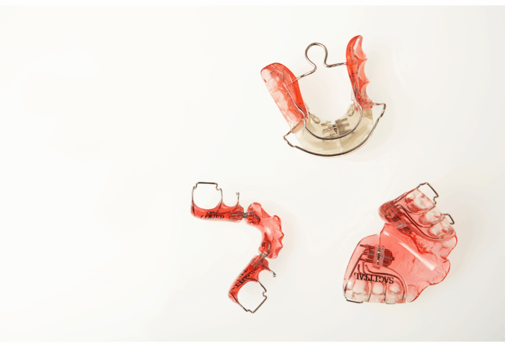 Three red orthodontic retainers, illustrating the appliances used for **maintaining a straight smile** after treatment at Manassra Dental in San Jose.