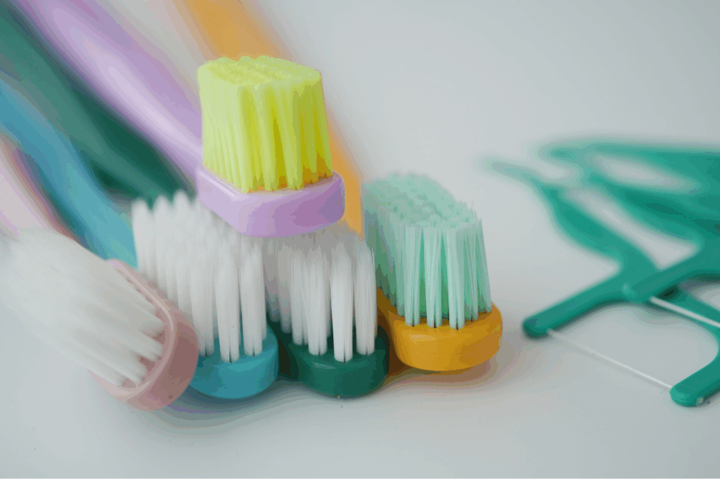 Colorful toothbrushes and dental floss picks, representing the essential tools for effective daily oral hygiene and **preventing gum disease** at Manassra Dental in San Jose.