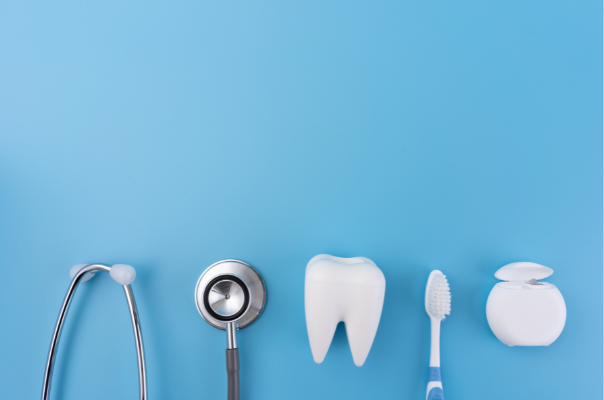 A stethoscope, a model tooth, a toothbrush, and dental floss arranged on a blue background, symbolizing the link between oral and physical health.