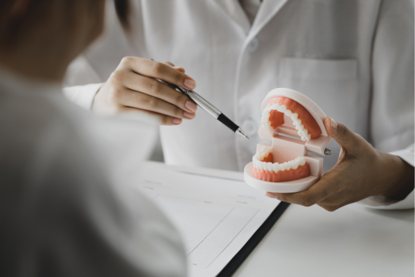 A dental professional at Manassra Dental using a 3D tooth model to explain a treatment plan to a patient during a comprehensive oral evaluation.