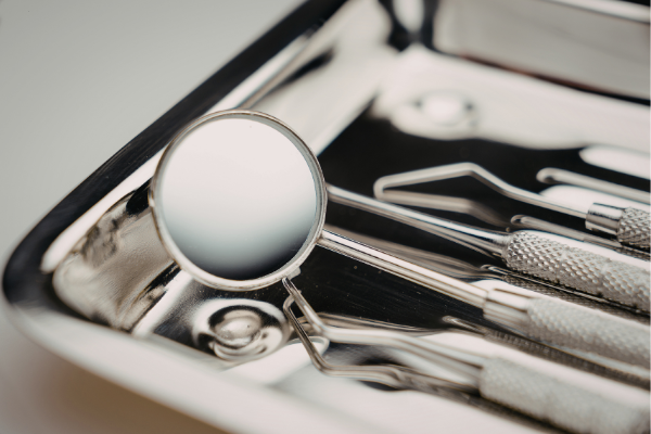 A stainless steel dental tray containing a sterilized mirror and various professional cleaning tools.