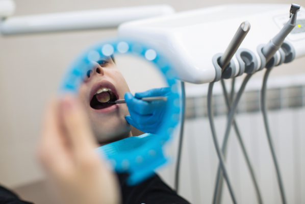 A dentist at Manassra Dental using a mirror and probe to perform a professional dental cleaning.
