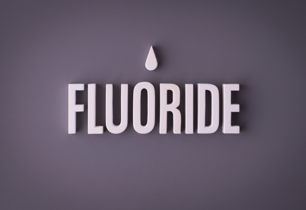 3D white lettering spelling "FLUORIDE" with a single droplet icon above it on a grey background.