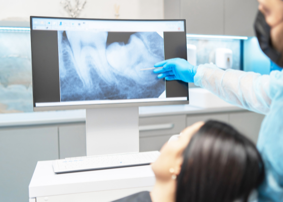 A dental professional at Manassra Dental pointing to a panoramic digital X-ray on a high-definition monitor while consulting with a patient.