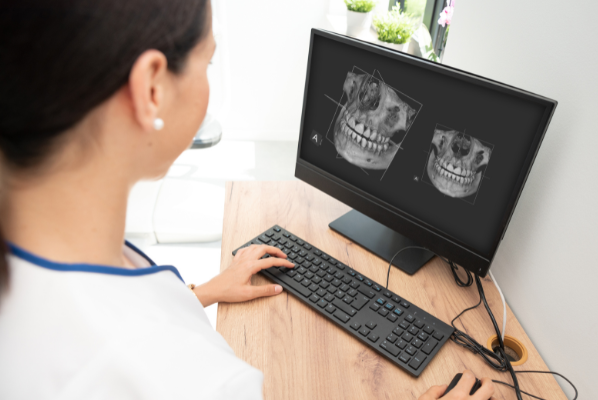 A dental professional at Manassra Dental reviewing a 3D CBCT bone and tooth reconstruction on a computer monitor.