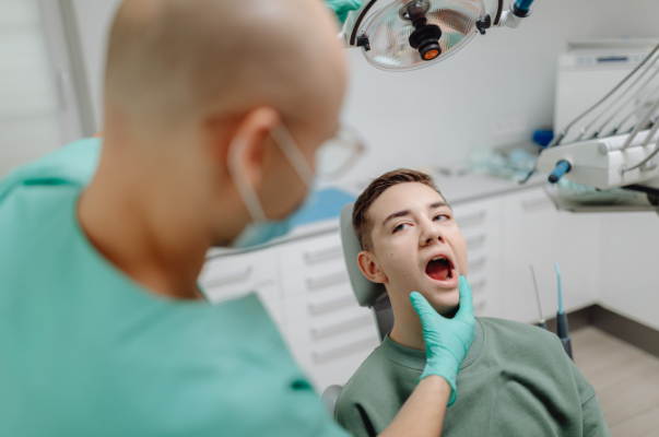 A dentist at Manassra Dental performing a manual neck and jaw palpation on a patient to check for oral cancer abnormalities.