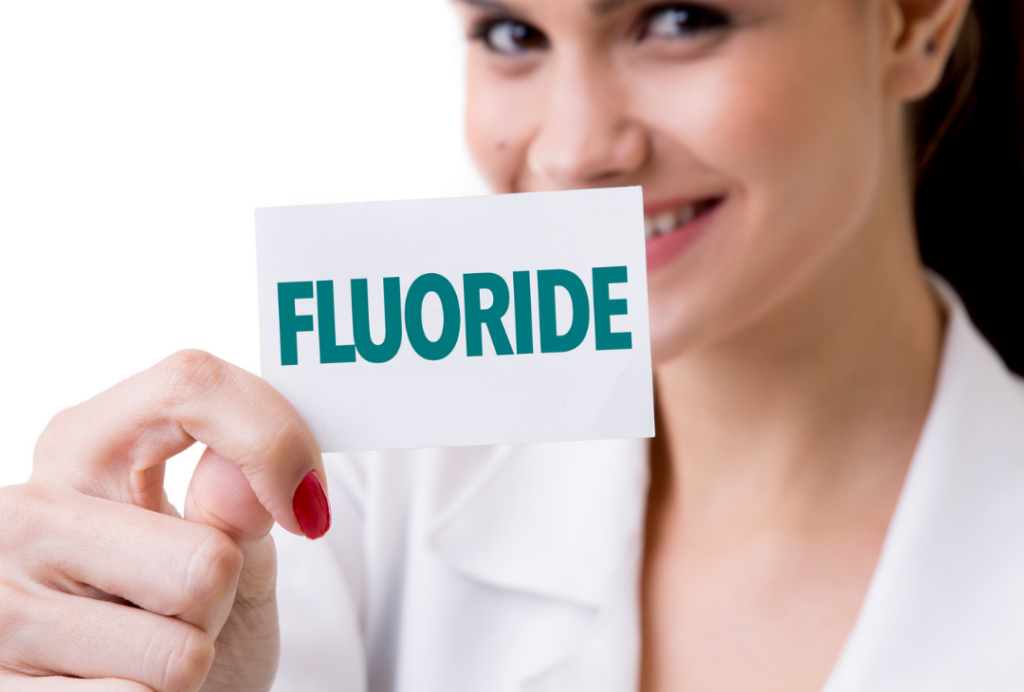 A dental professional at Manassra Dental holding up a card that says "FLUORIDE."