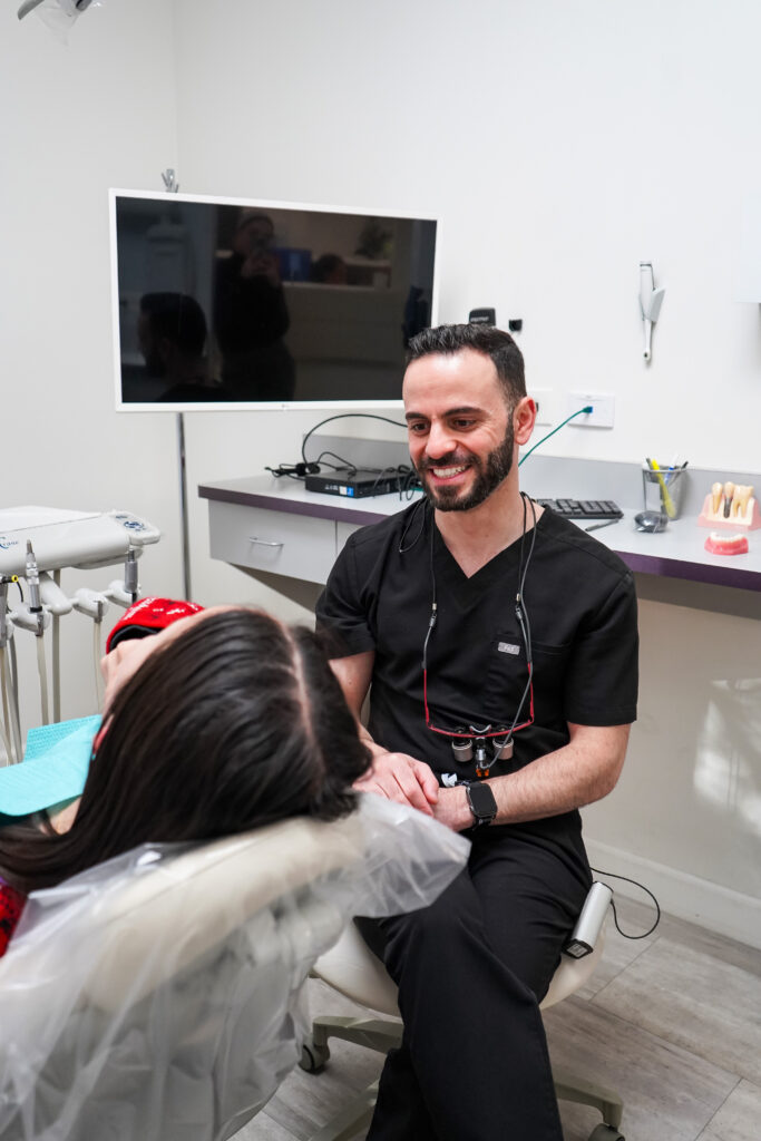 Dr. Manassra smiling while discussing a custom teeth whitening plan with a patient in a modern dental office.