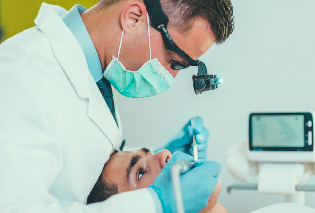 A dentist at Manassra Dental performing a root canal procedure using a dental microscope and specialized lighting.