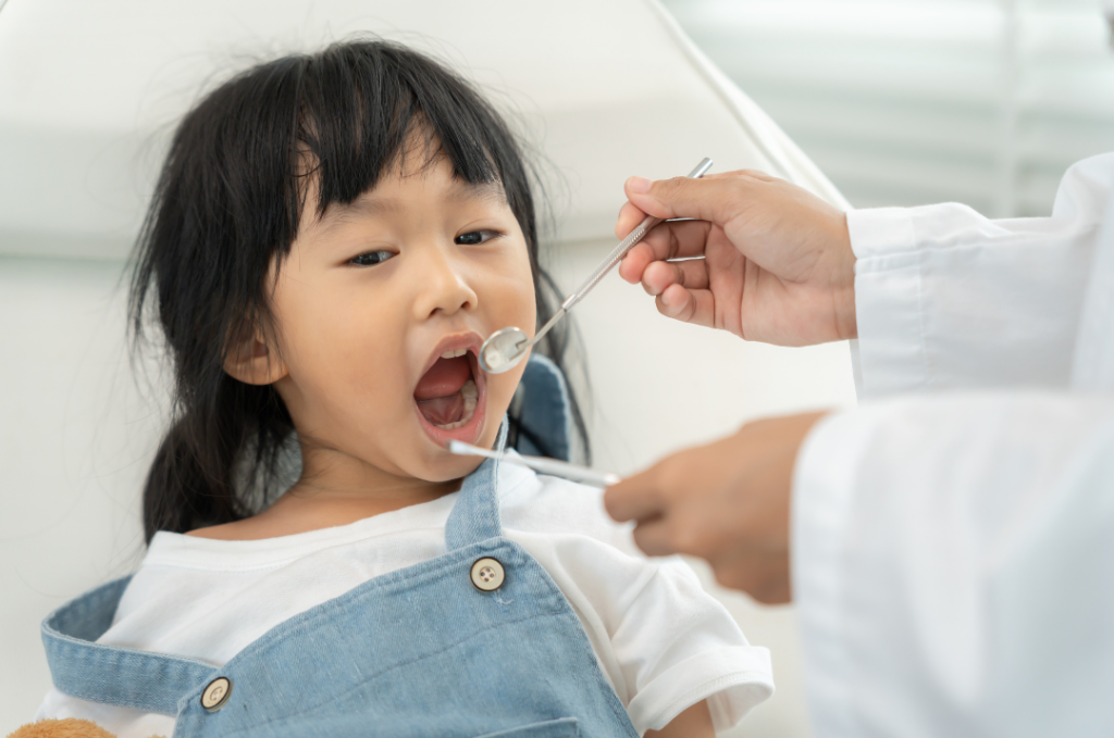 A young girl with her mouth open during a dental exam at Manassra Dental while a professional uses a mirror and probe.